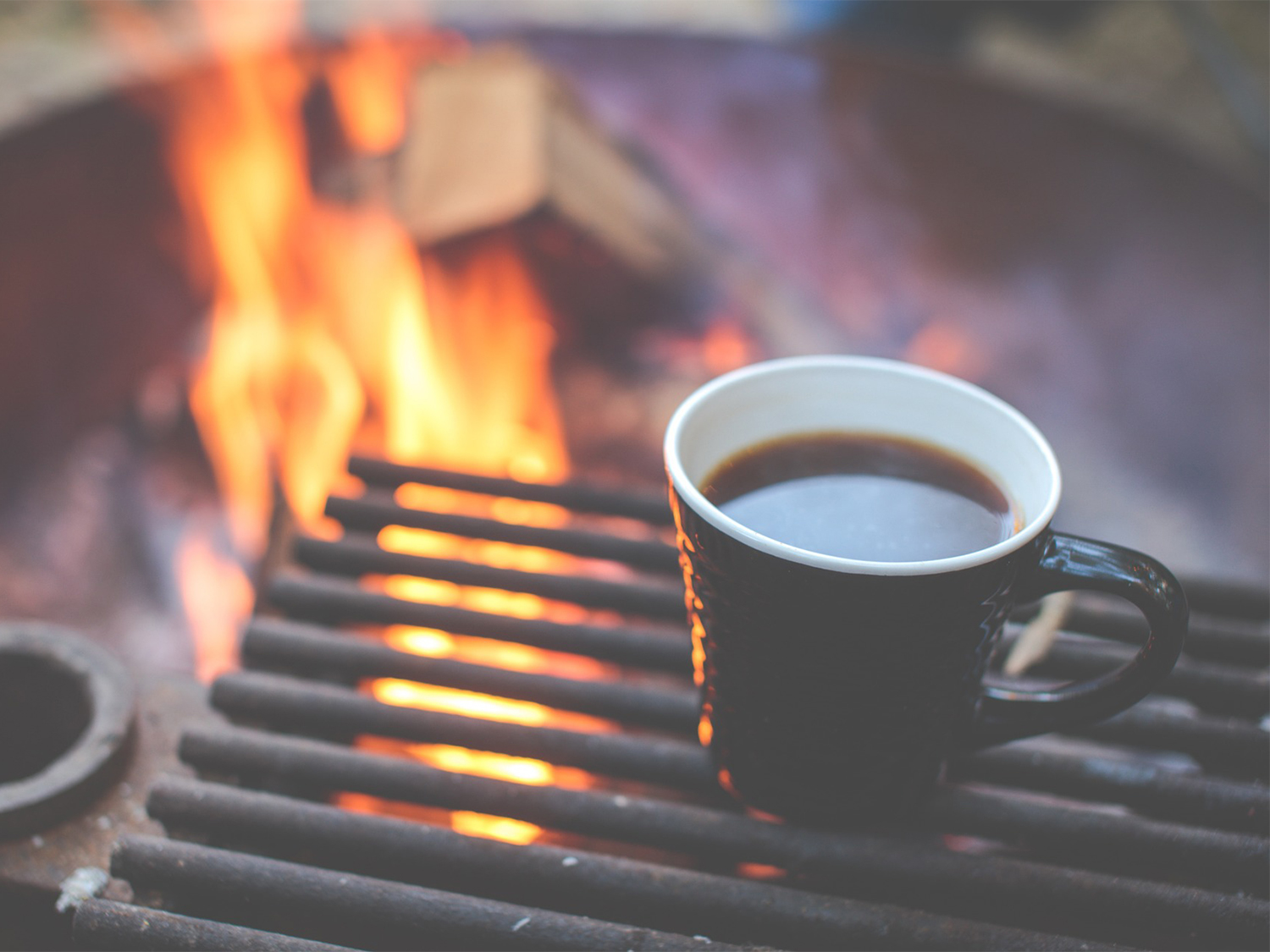 A cup of coffee beside a campfire.