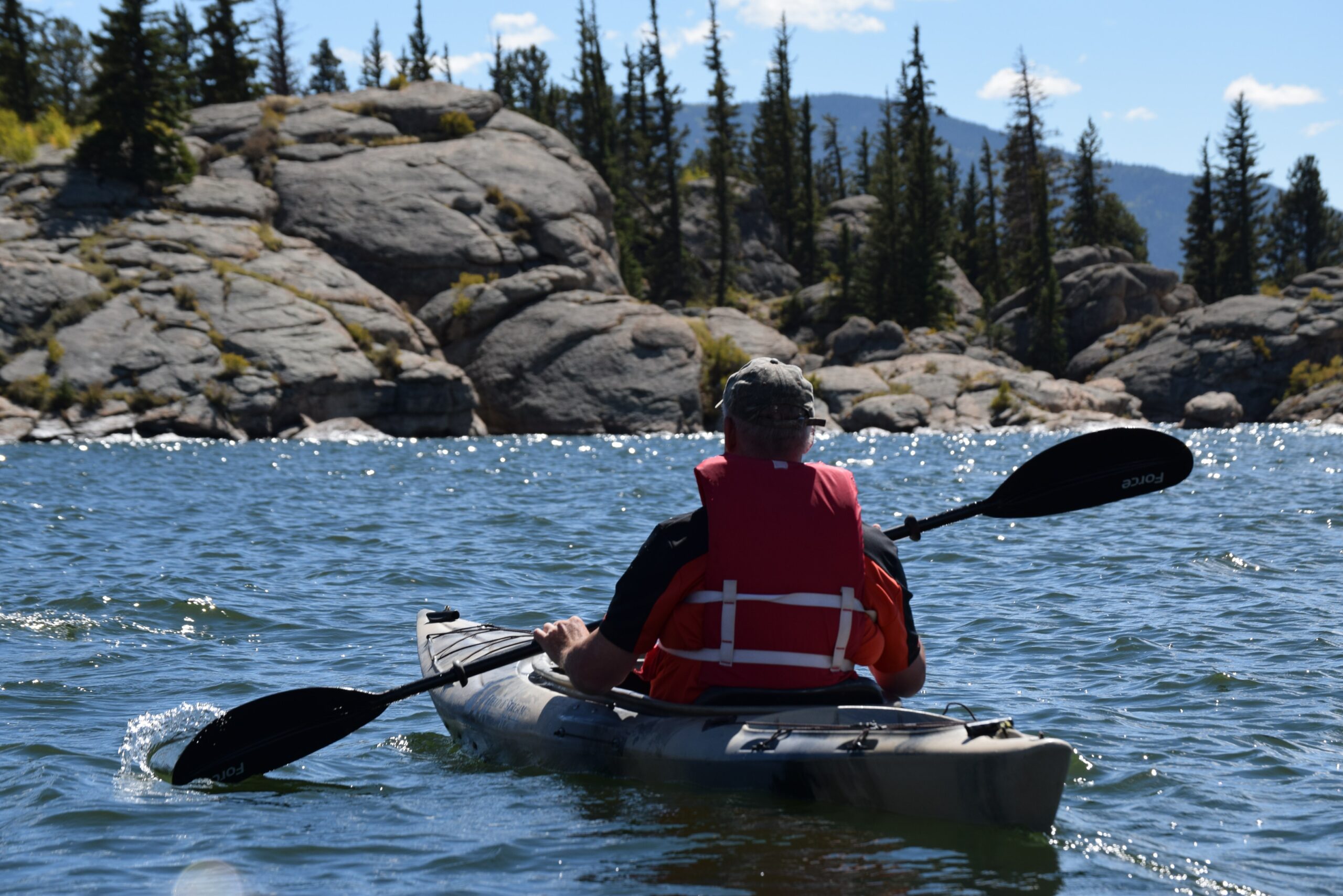 A person kayaks in the waters of the wilderness wearing the best fishing life vest.