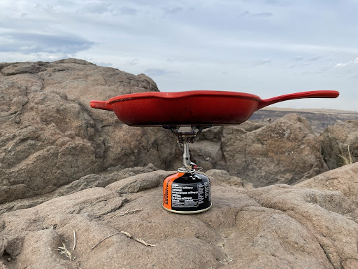 A red cast iron pan on a small backpacking stove