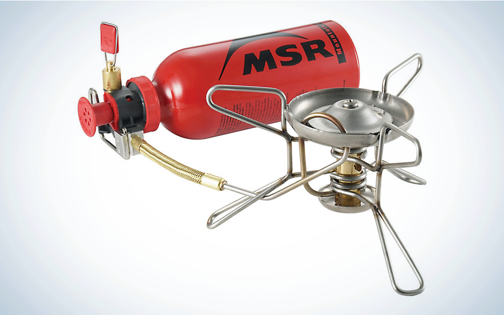 A silver backpacking stove with a red fuel bottle