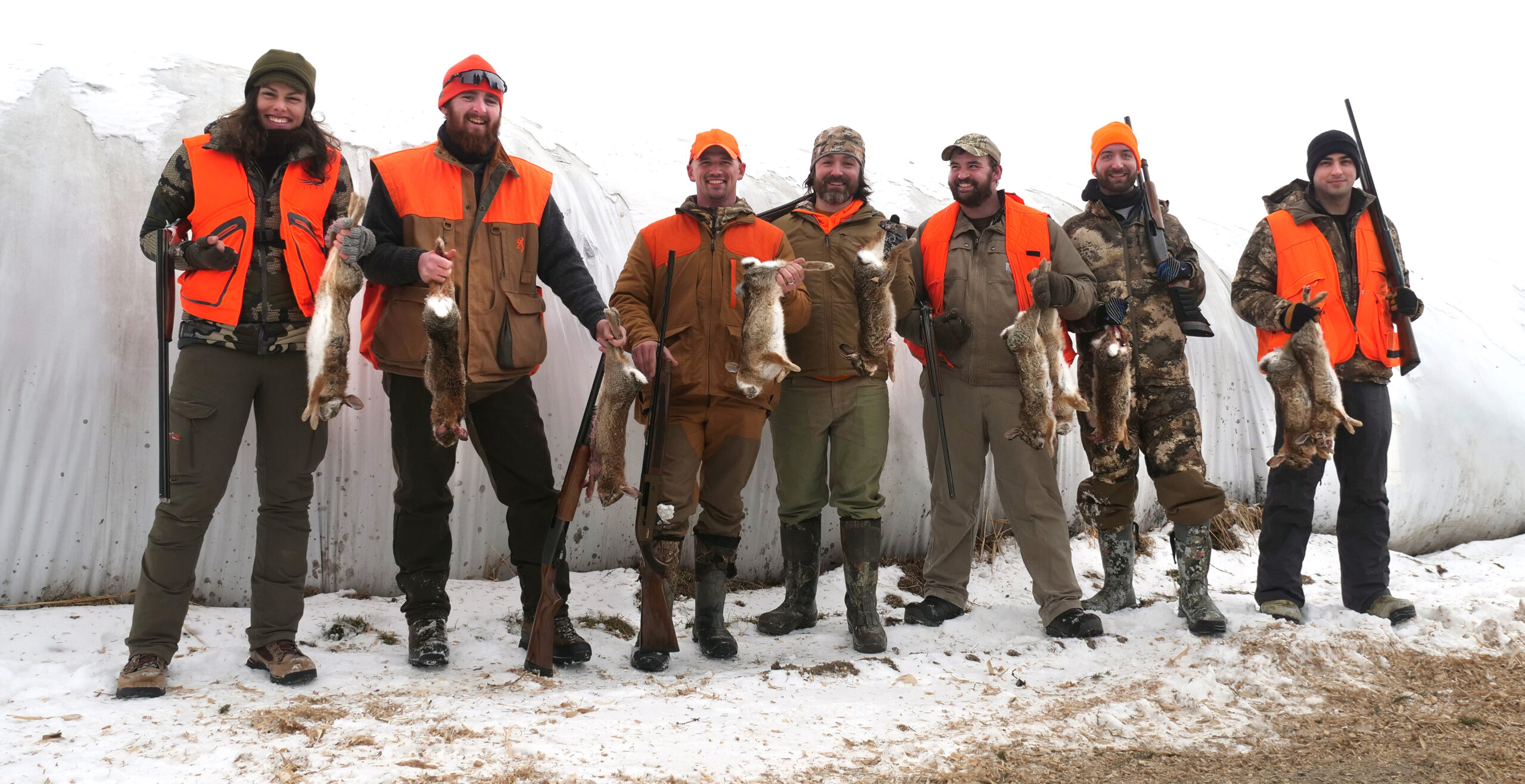 A group of happy rabbit hunters in blaze orange and camo on a snowy day.