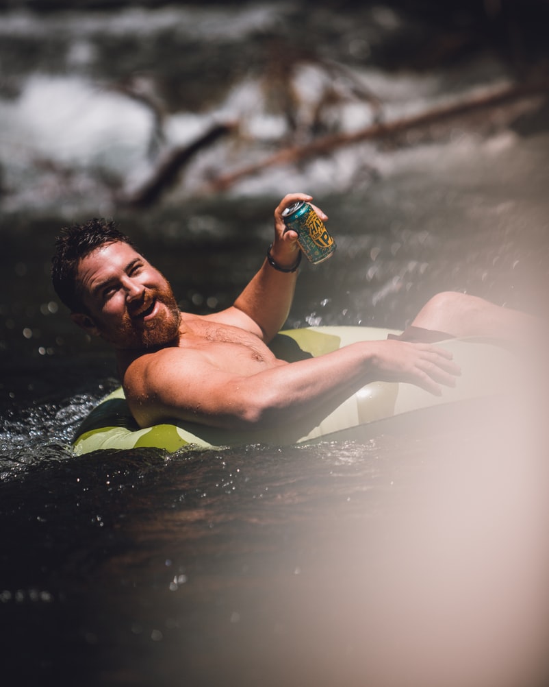 A man in a float tube smiling and drinking a can of beer.