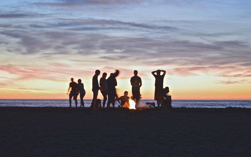 A group of people around the fire during sunset into the beach.