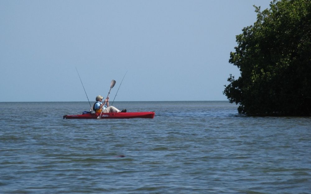 A man with hat on kayak sailing on the blue sea.