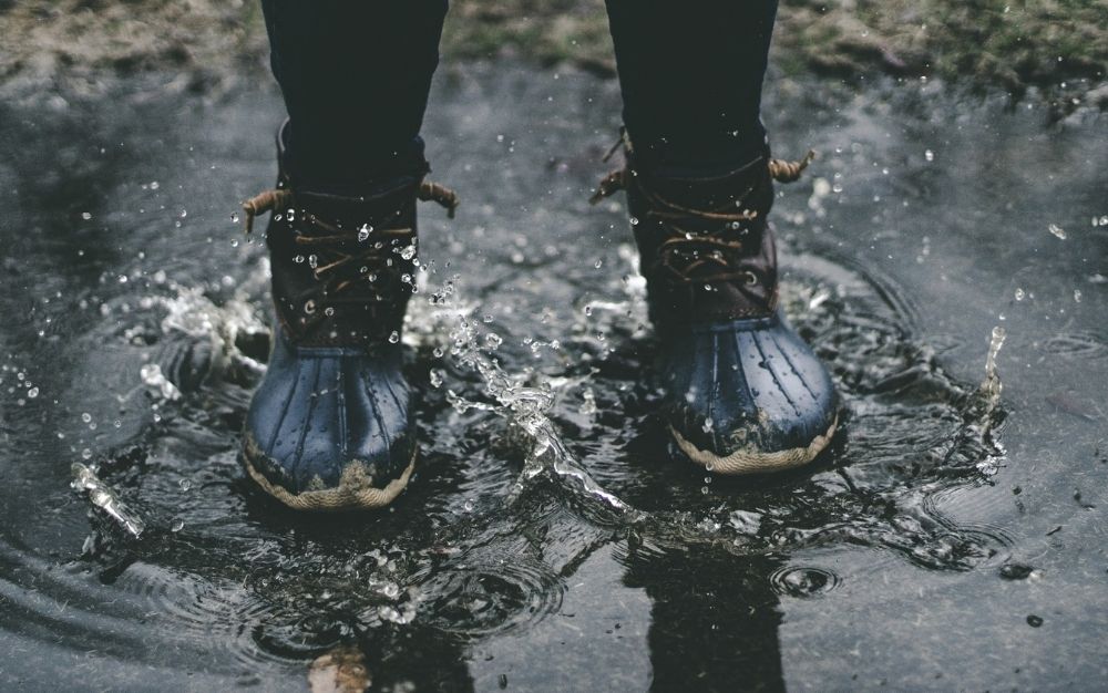 Woman wearing blur rubber sole boots with laces for fastening standing on splashed water.
