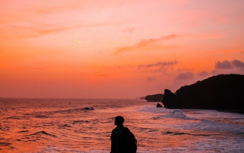 A man standing by the sea and watching the sunset.