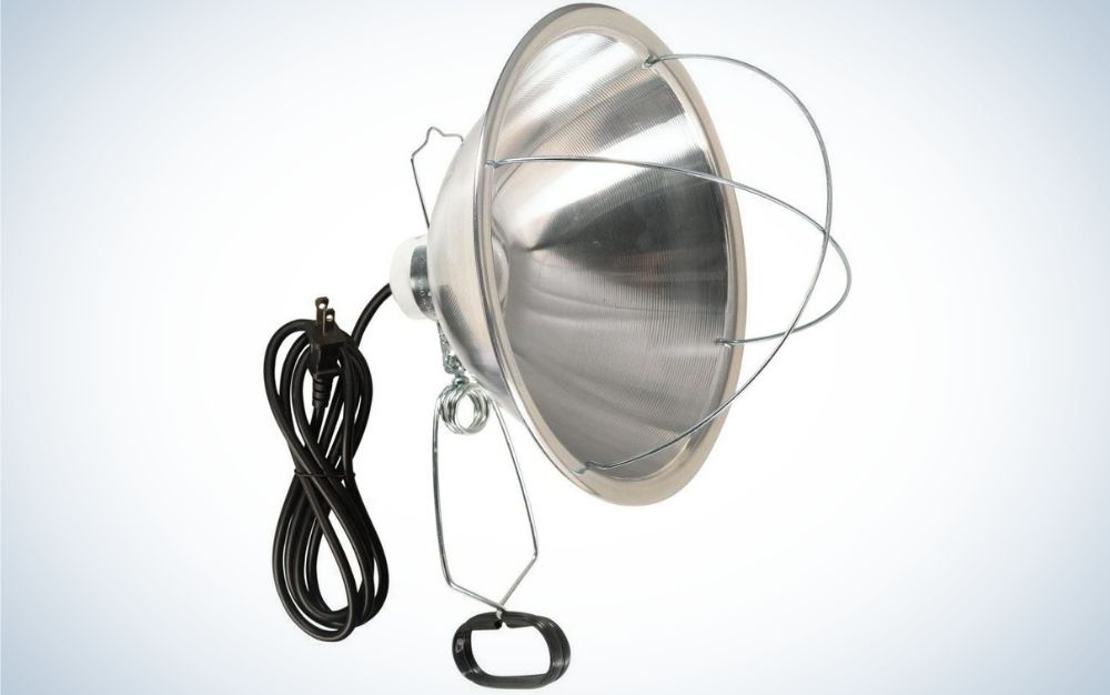 A large lamp with reflector all in silver color and with some wires crossed in front of it, as well as with a black plug.