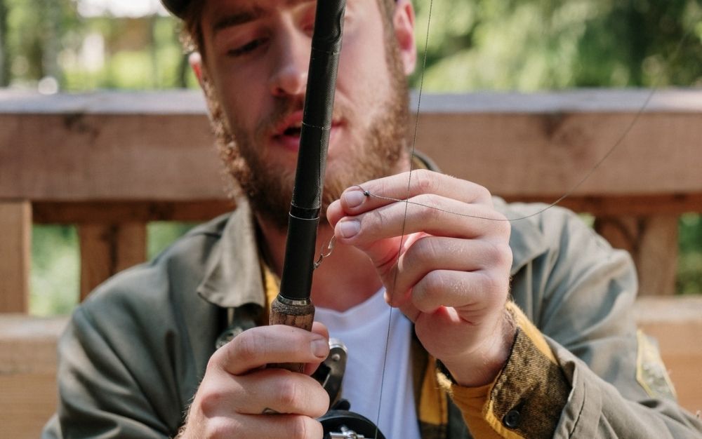 A bearded man wearing a green jacket who is arranging a black spinning rod.
