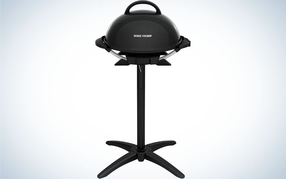 A black electric grill in a circular shape with a long stick and four moving wheels.