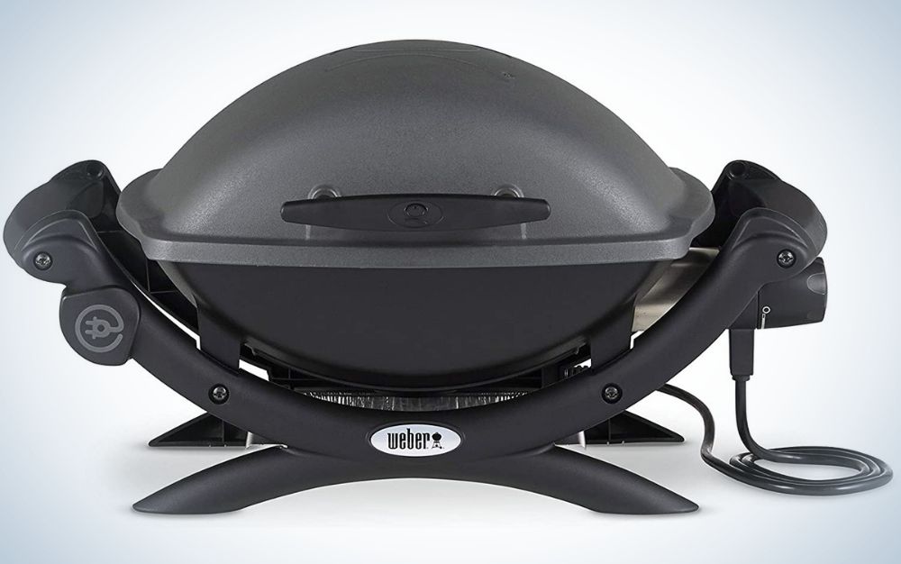 A black electric grill in a circular shape and assembled with two support legs on the ground.