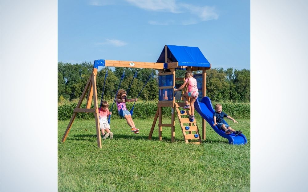 Four children playing in an outdoor playground on a grassy field, two children do the laundry, one climbs the stairs and the other is on the sidewalk.
