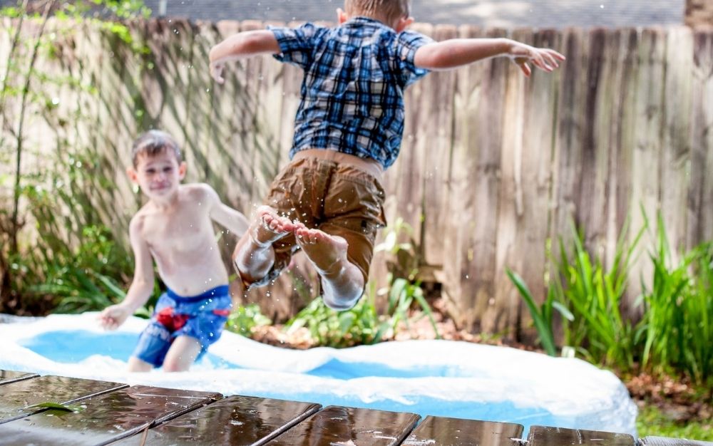 Two boys playing into a outdoor swimming pool and one of them is jumping into the pool water.