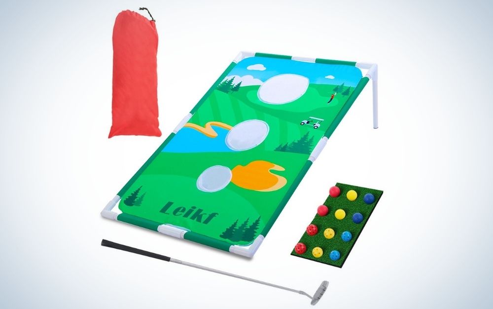 A portable golf backyard in solid green with a few holes in it, as well as a red bag and a box of golf balls and a golf club.