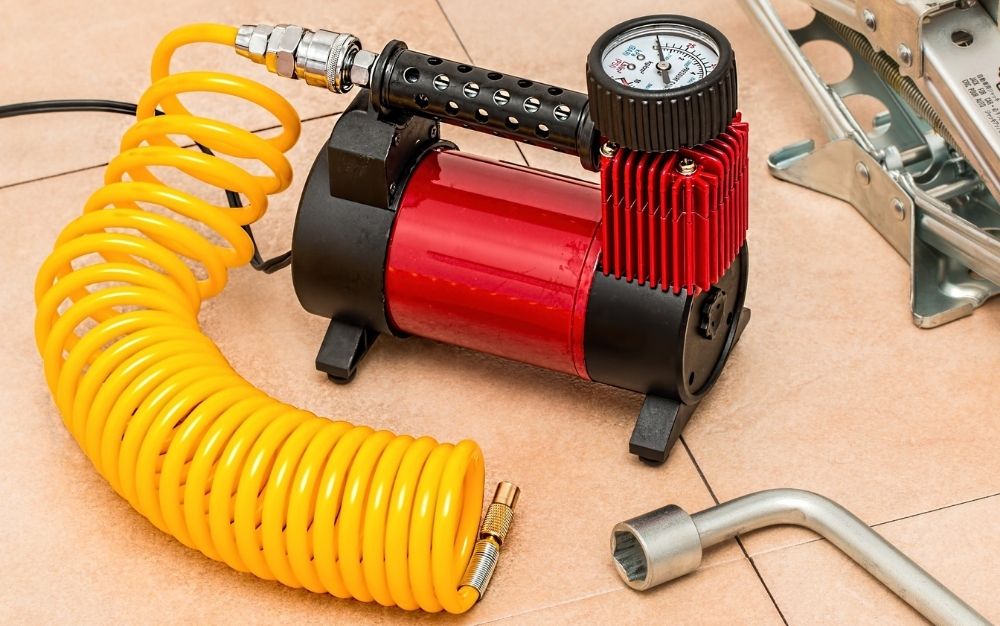 An air compressor on the ground with some beige plates and a yellow circular tube.