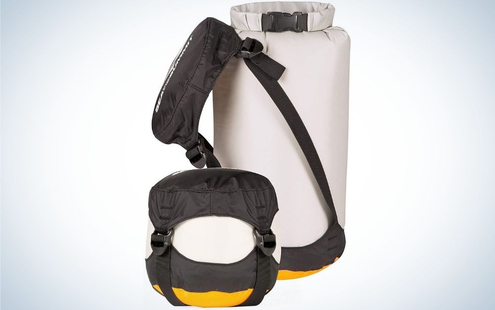 A large bag similar to a boxing bag which is white in color and in the shape of a cylinder, next to it are a waist bag with a long black belt and a small square bag of different colors.