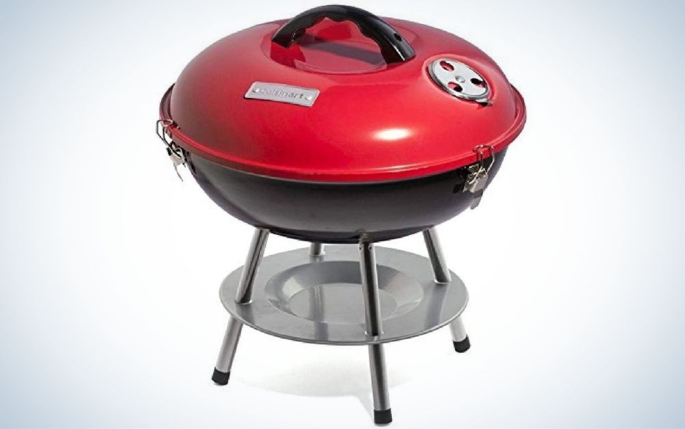 A portable grill in the shape of an oval and quite wide red color, under it a gray aluminum part placed below the red grille, as well as the gray support floor.