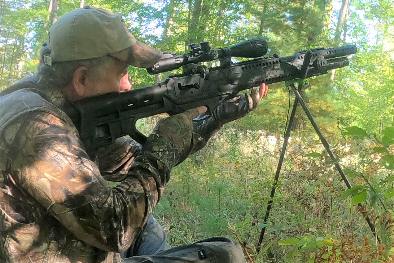 A man shooting a black air gun in the woods