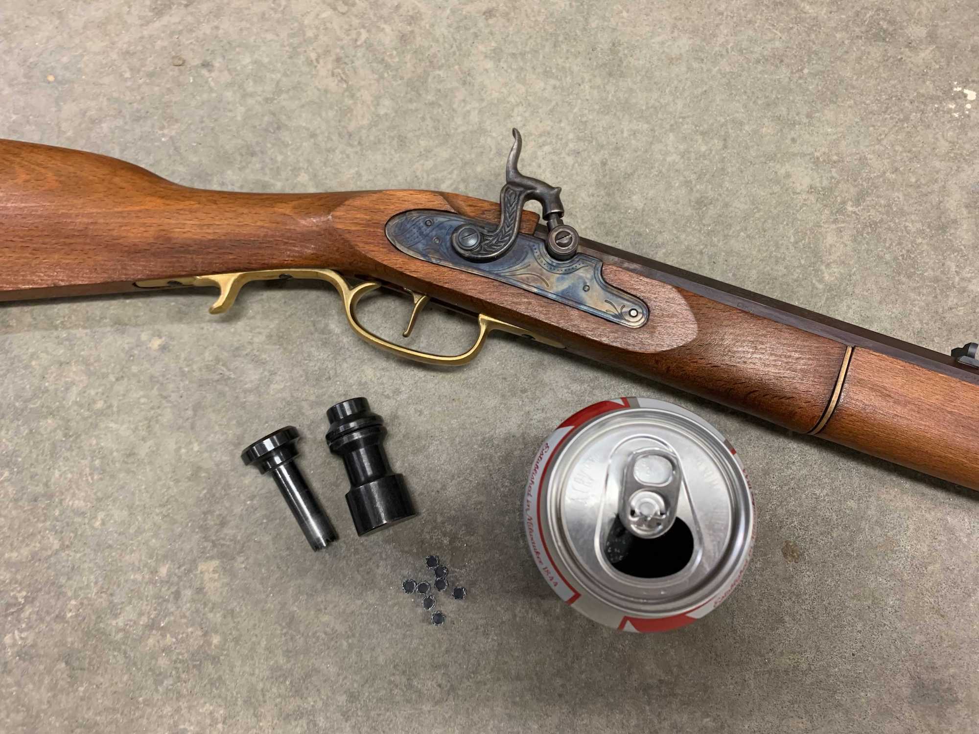 A muzzleloader next to an aluminum can and two percussion cap makers