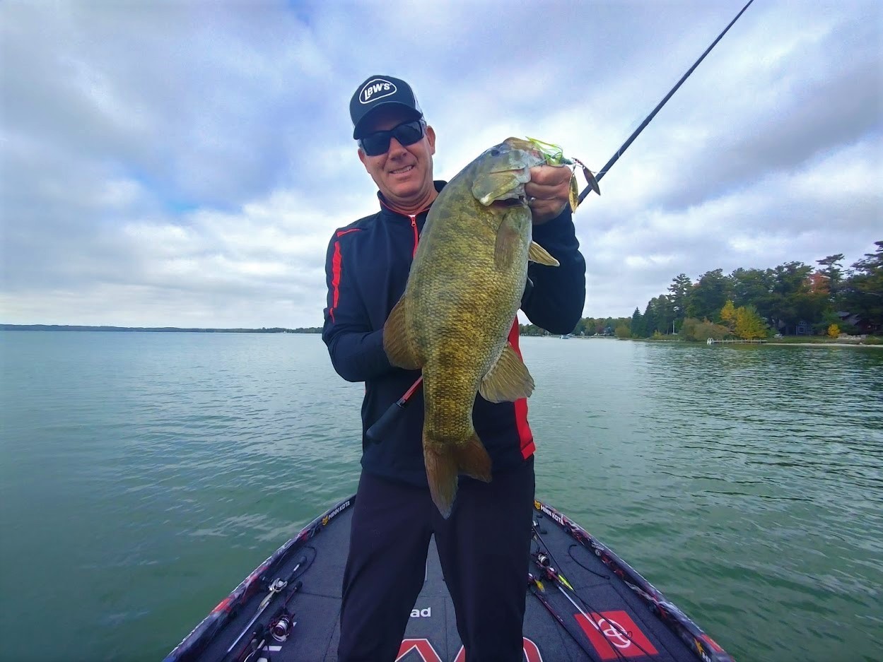 A man on a boat on the water holding a smallmouth bass