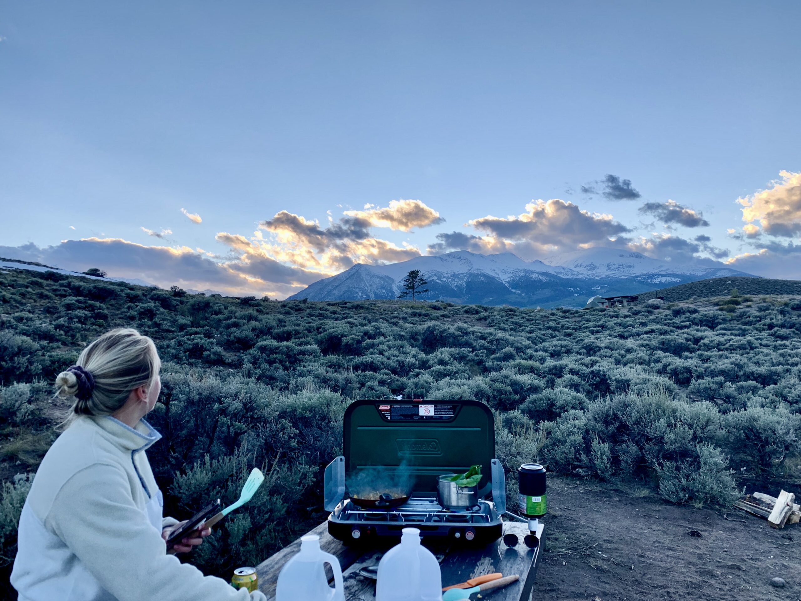 A woman cooking on a camping stove looking over mountains