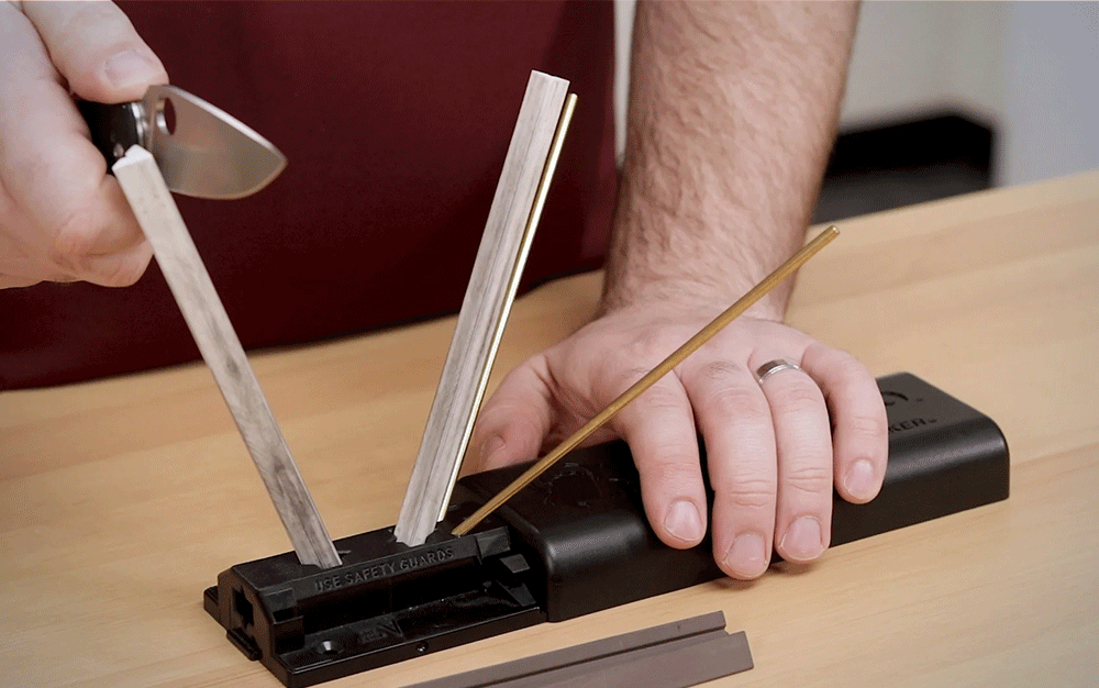 A person sharpening a knife on a black and silver sharpener