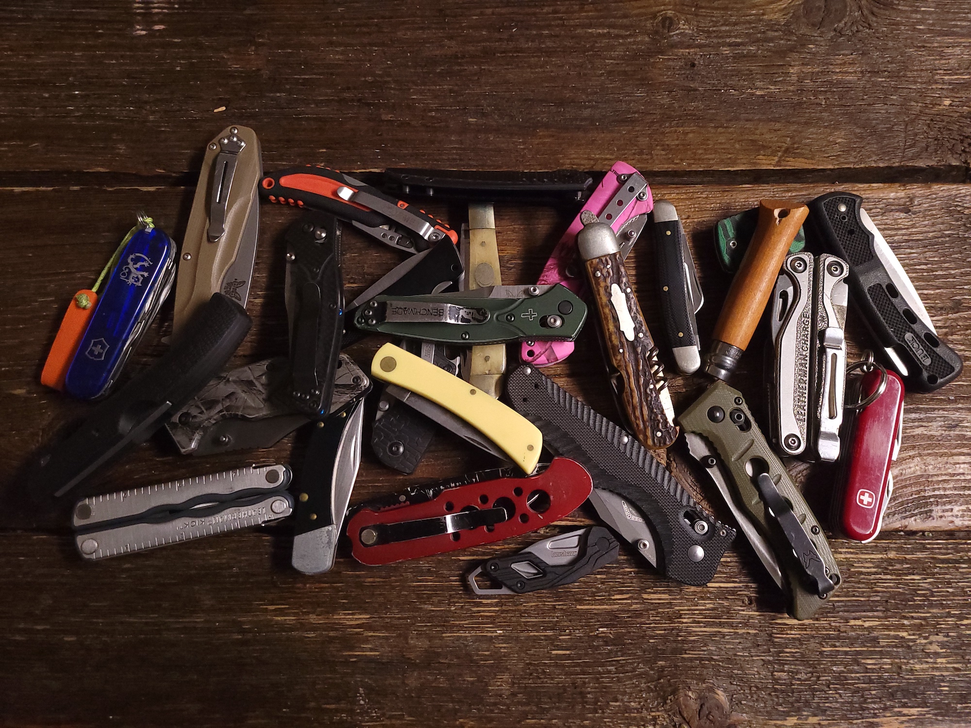 A pile of pocket knives on a wooden surface