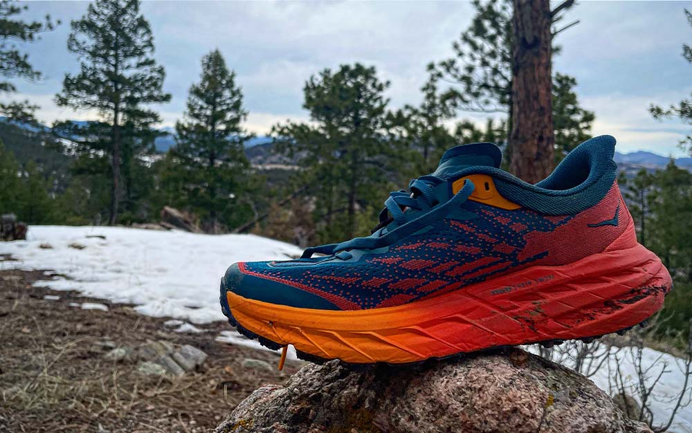 A blue and orange best trail running shoe on a rock next to a snowfield