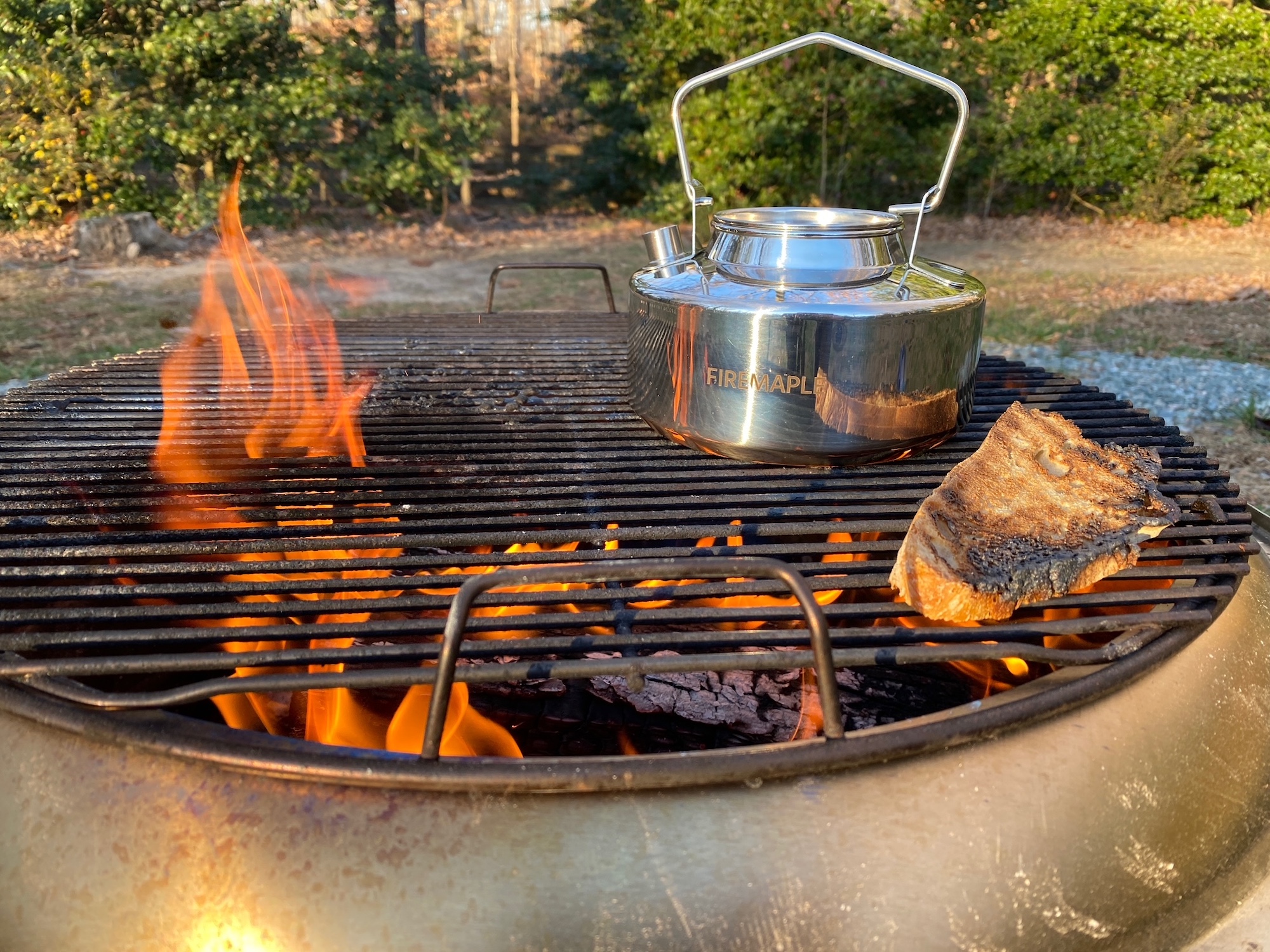 A kettle and piece of bread over a fire pit flame