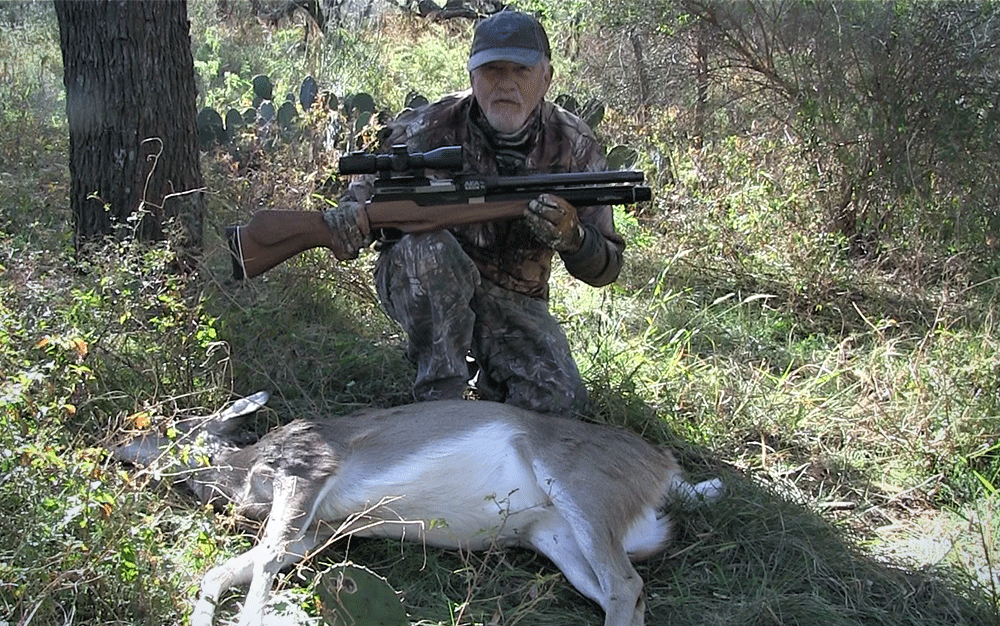 A man holding an airgun kneeling over a dead deer