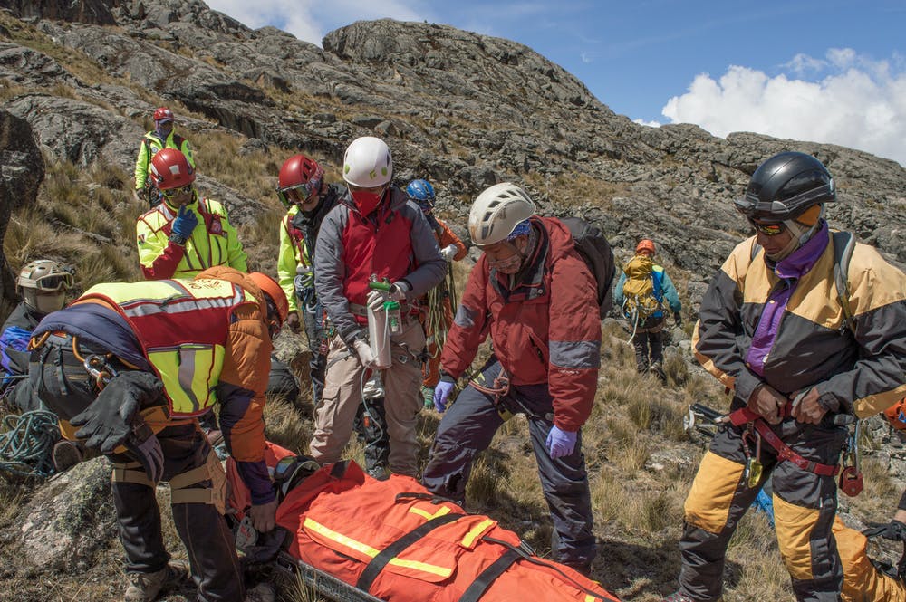 A group of rescuers on a mountain standing over someone in a litter