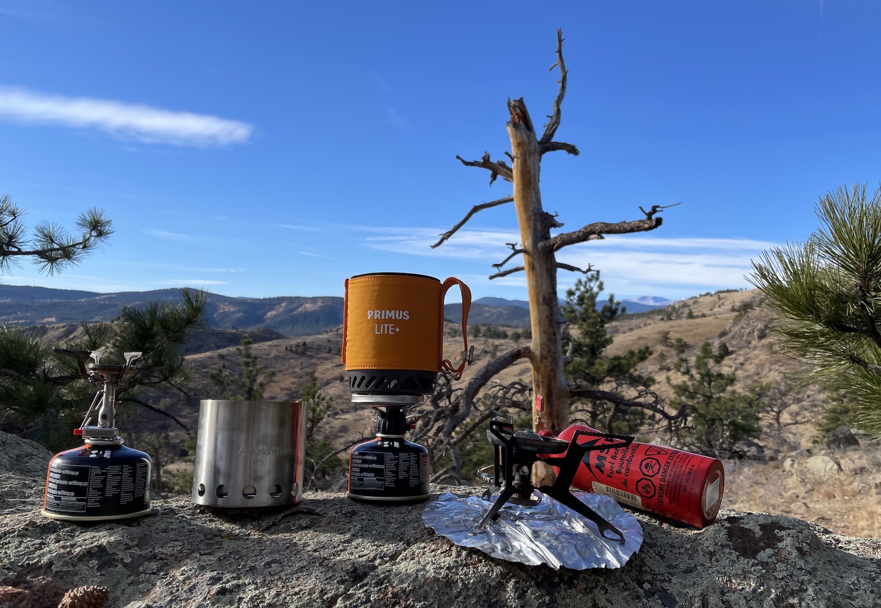 Four of the best backpacking stoves sitting on a rock with blue skies