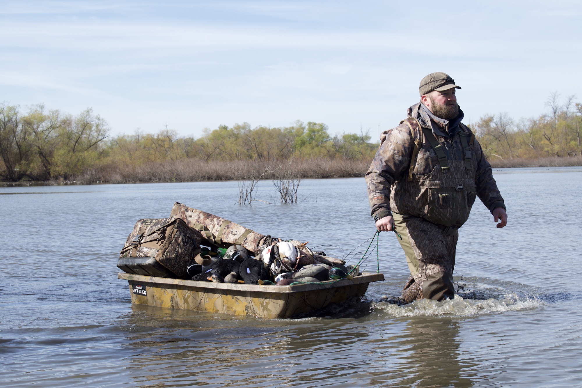 A man wearing one of the best waders for duck hunting dragging gear through the water