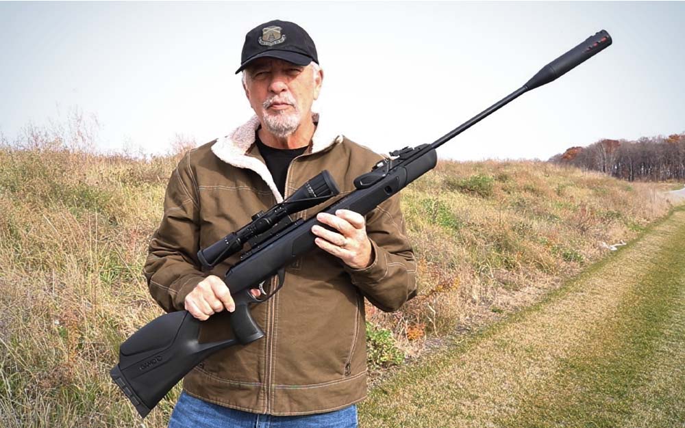 A man holding a black air rifle in a field