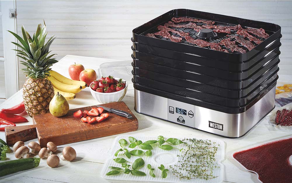 A black dehydrator with jerky next to piles of fruit