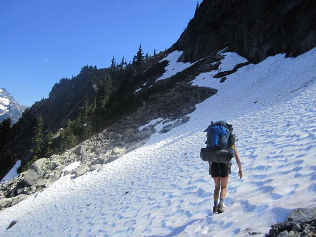 A person wearing a large blue backpack crossing a snow field
