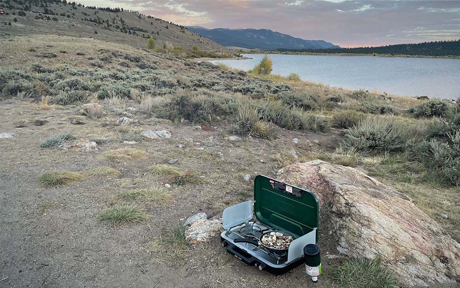 A green camping stove on a lake's beach