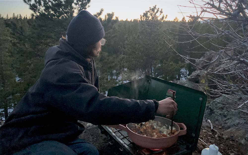 A person cooking on a green stove at sunset