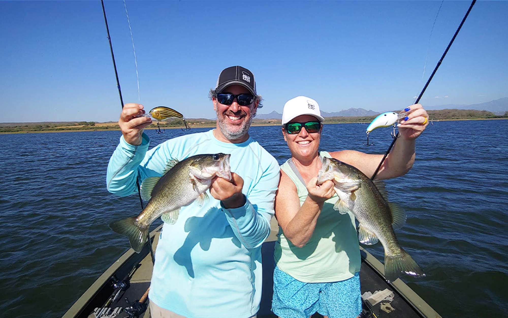 A man and a woman on a boat holding fishing rods and bass