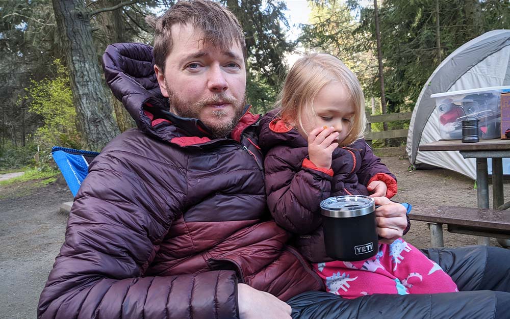 A man and a child in matching purple coats holding a best camping mug