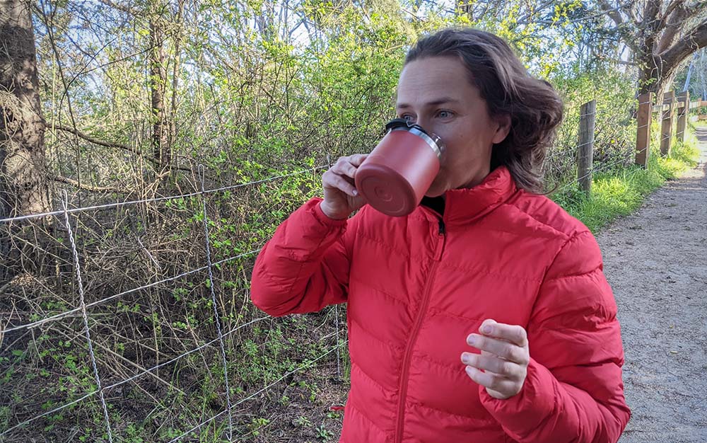 A woman outside in a red jacket sipping from a red best camping mug