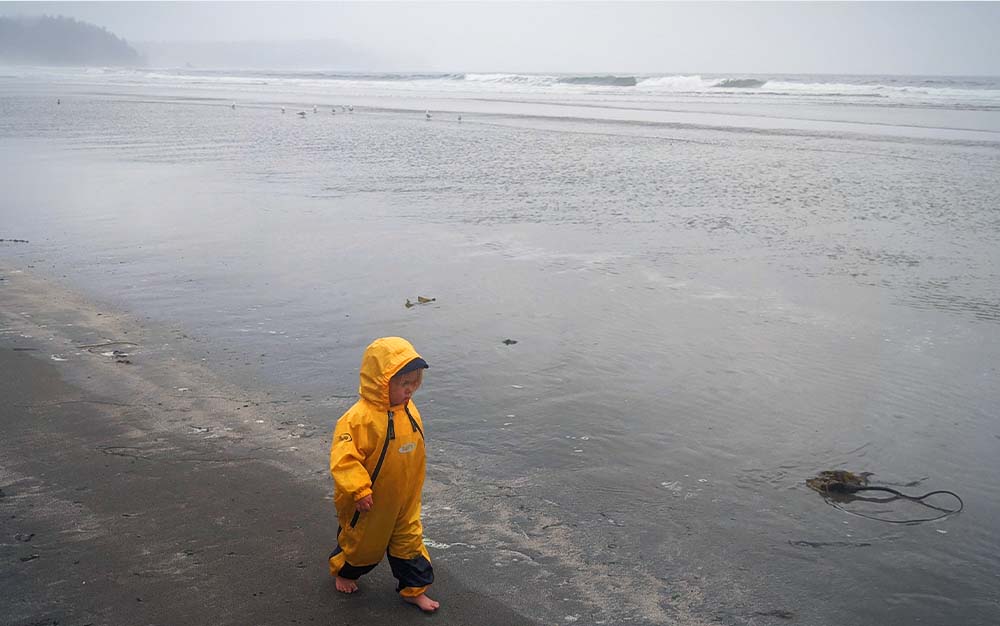 A child wearing a yellow rain jacket on a beach