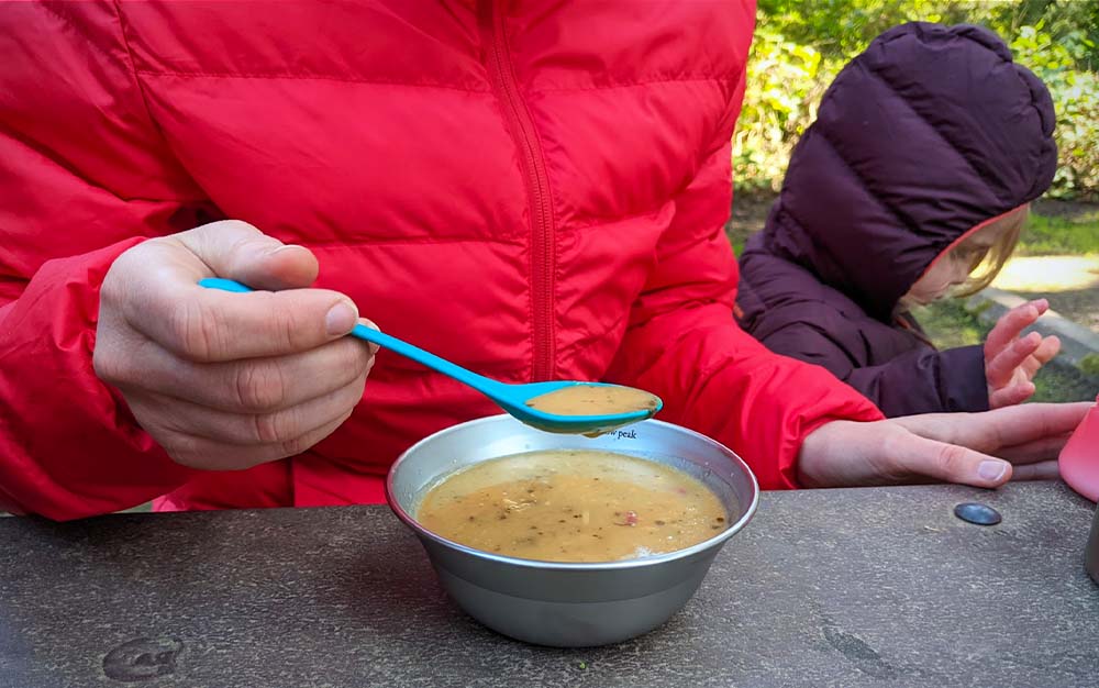 A woman holding a blue spoon eating soup
