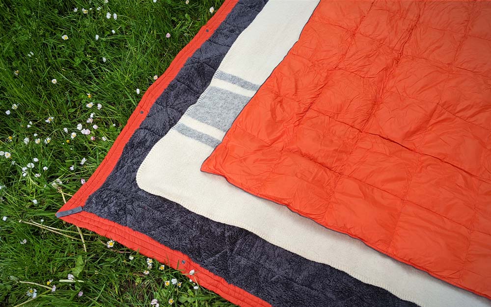 Different materials provide different functionality in the outdoors and require different care. From top to bottom, the Get Out Gear Down Puffy Camping Blanket, the Ibex Wool Blanket, and the Kammok Mountain Blanket, which has a fleece underside.