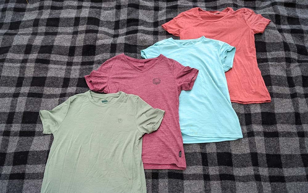 Four of the best hiking shirts laid out on bed.
