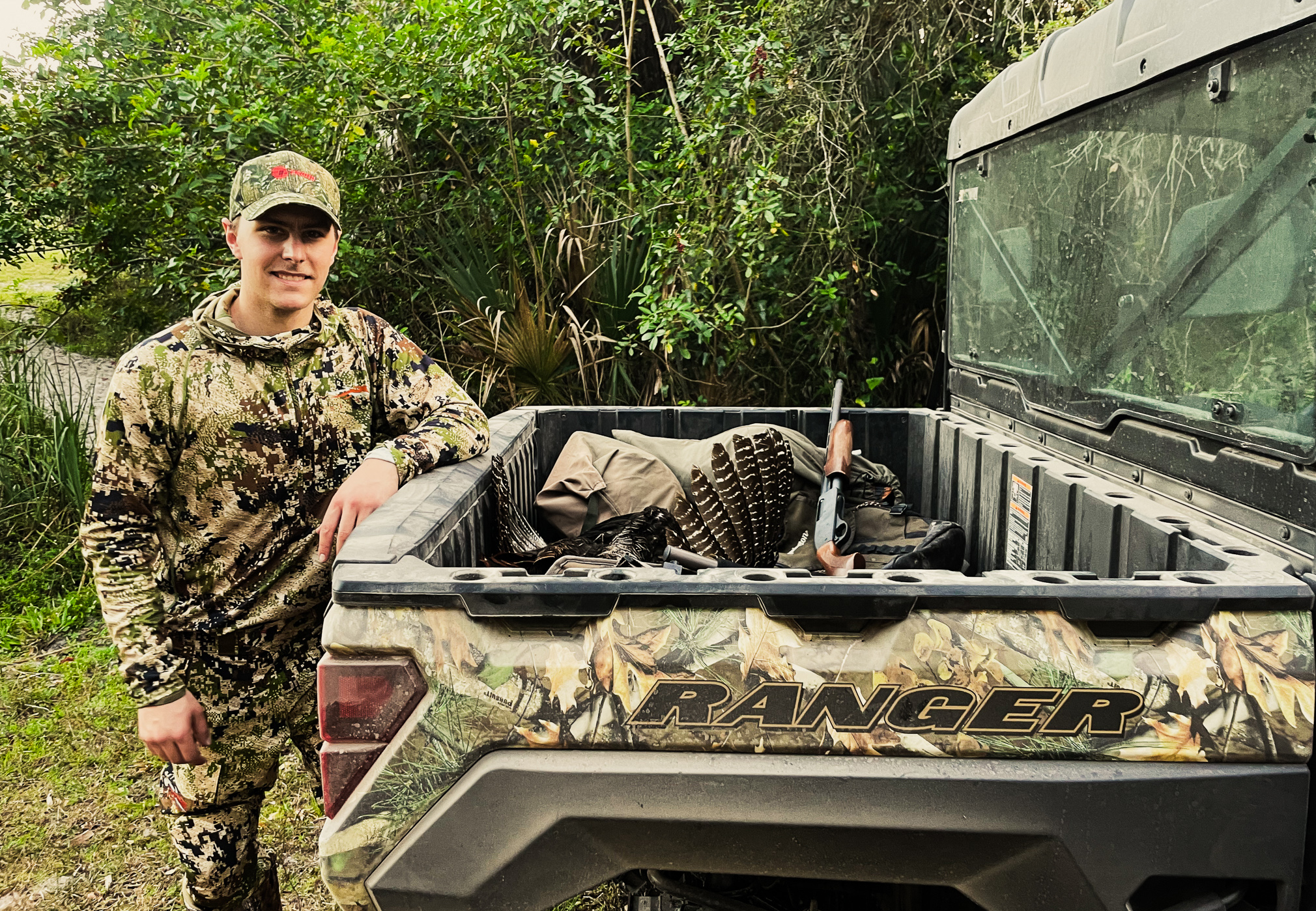 A turkey hunter leans against the tailgate of the Polaris Ranger Kinetic.
