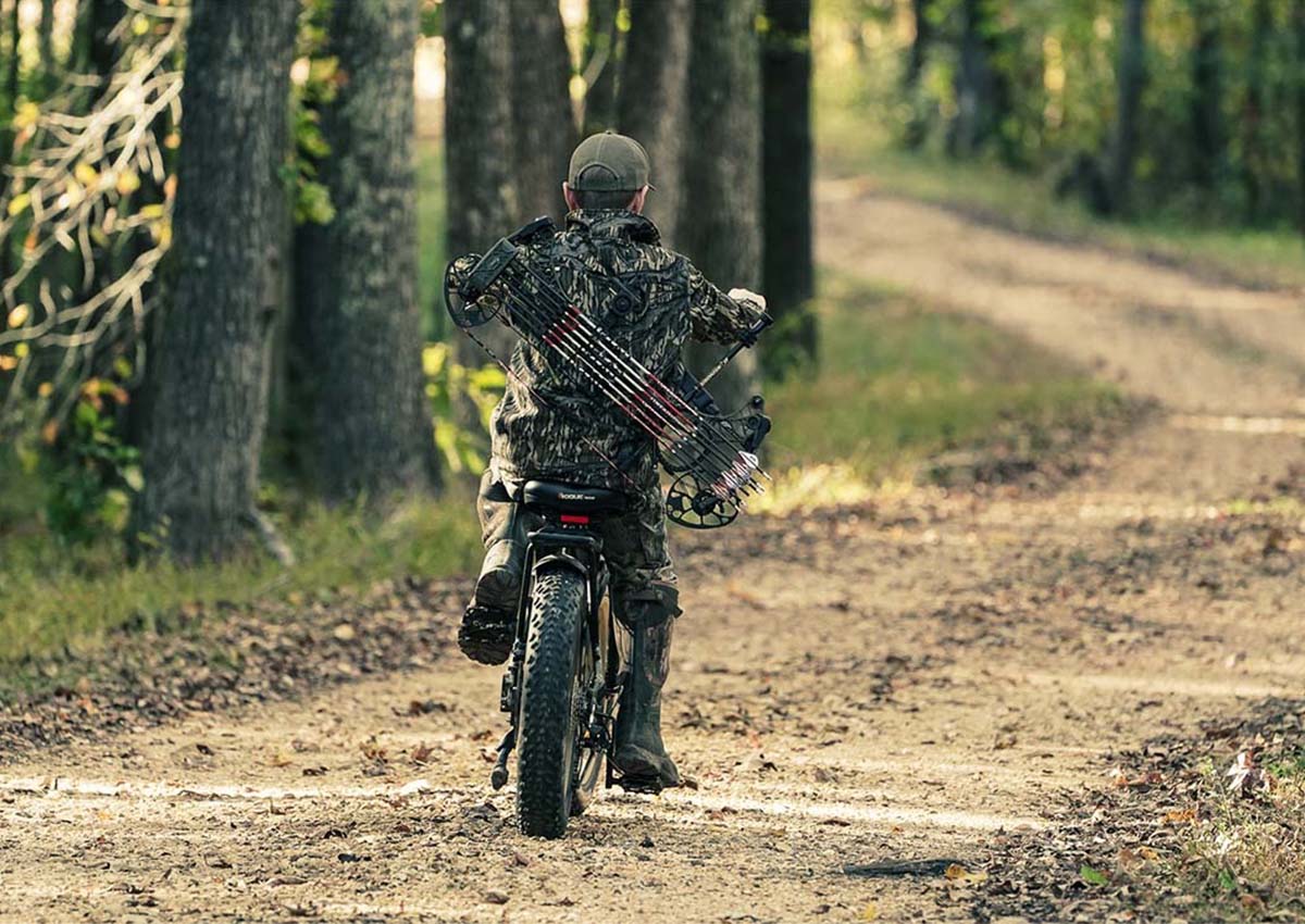 A bow hunter ride an electric bike down a forest trail.