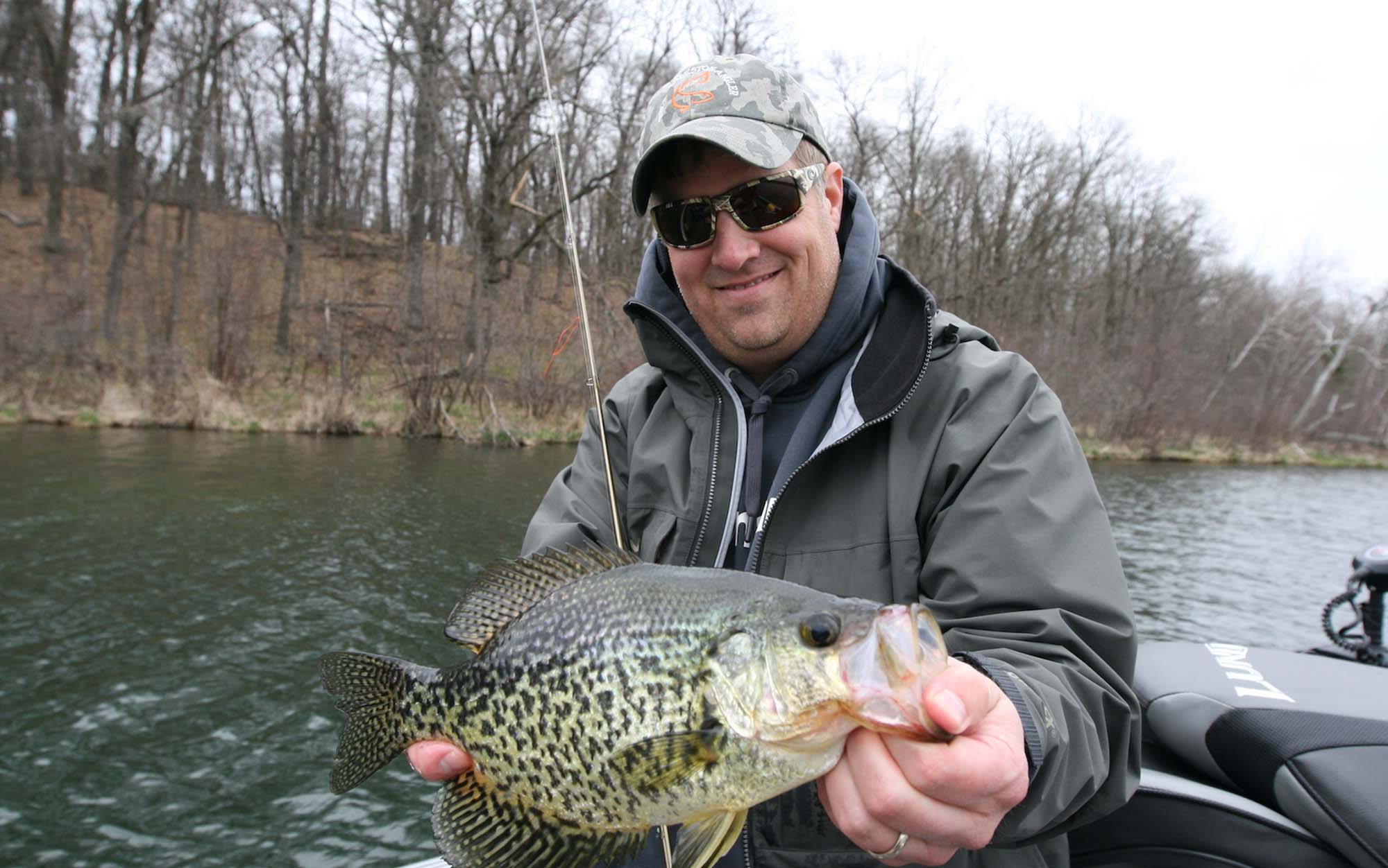 Man holding crappie in a fishing boat.