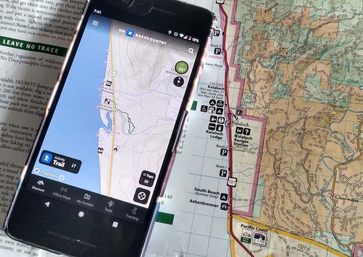 The OnX Backcountry App lying on top of a paper map.