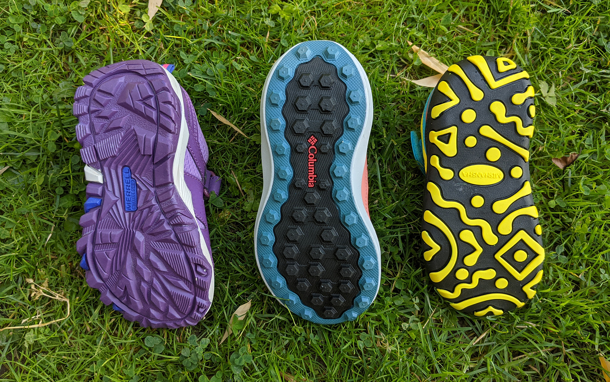 The bottoms of the best hiking shoes for kids laying in the grass.