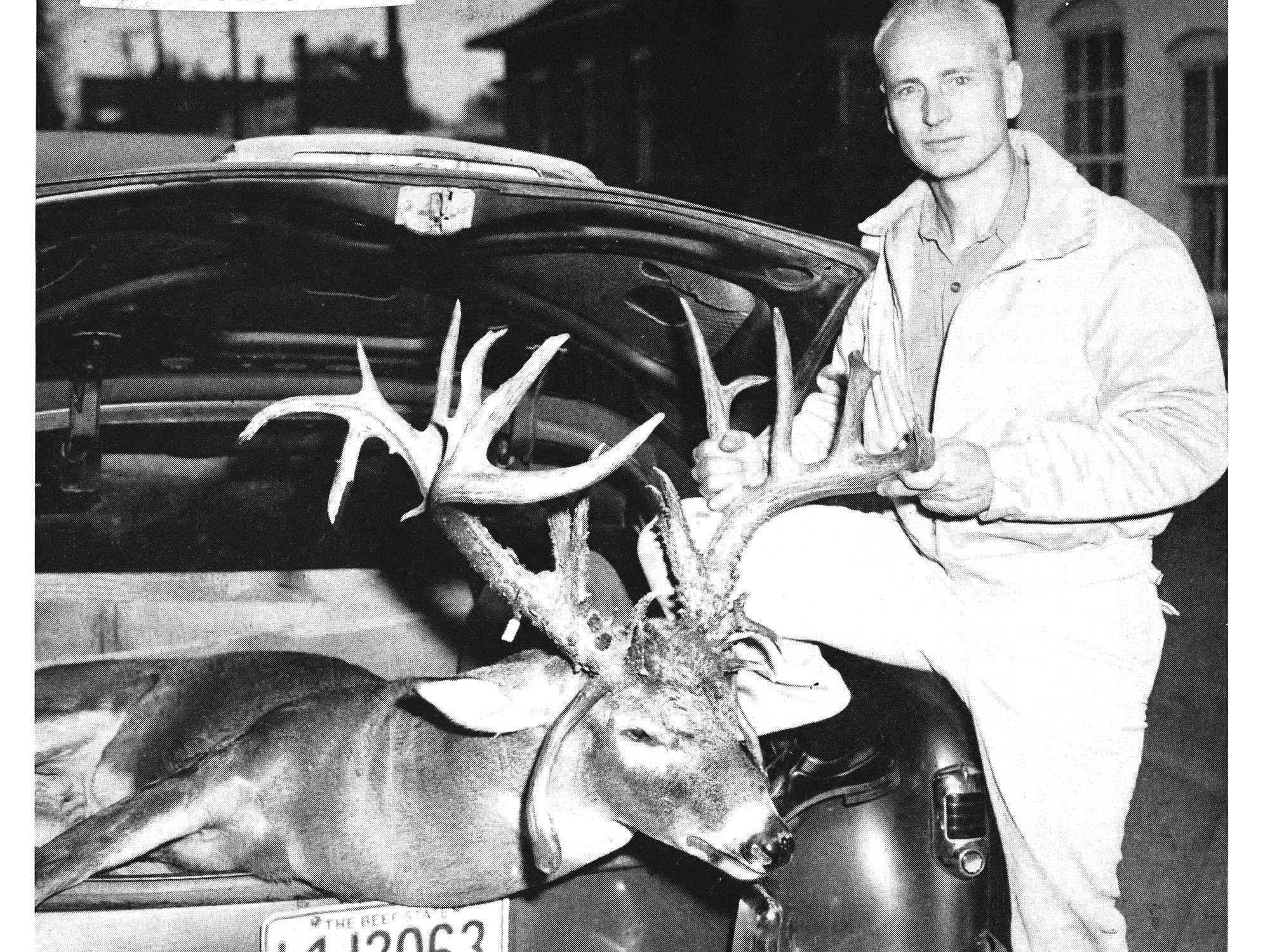 B&W photo of hunter with deer in trunk